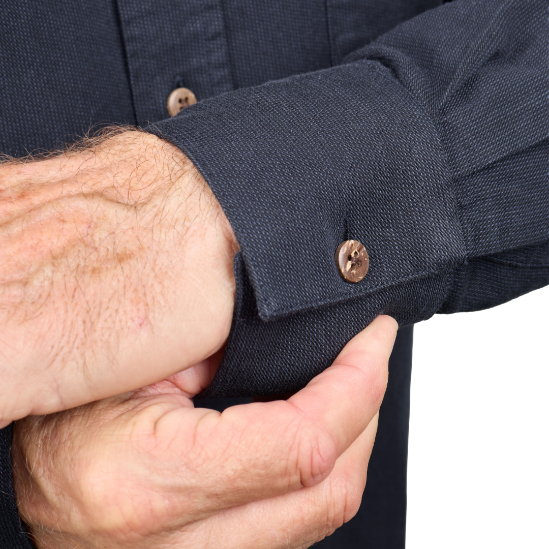 Close-up of a person's hands adjusting the cuff of a dark navy blue textured long-sleeve shirt, showing a brown button closure.