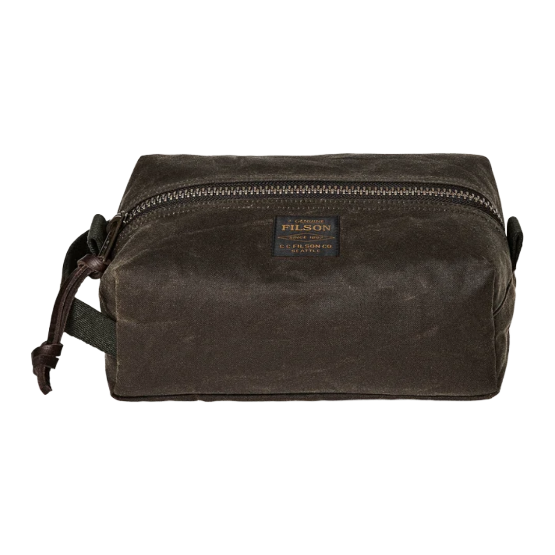 A dark brown waxed canvas pouch bag with a top zipper, a small rectangular Filson brand patch on the front, and a dark strap on the left side, shown against a plain white background.