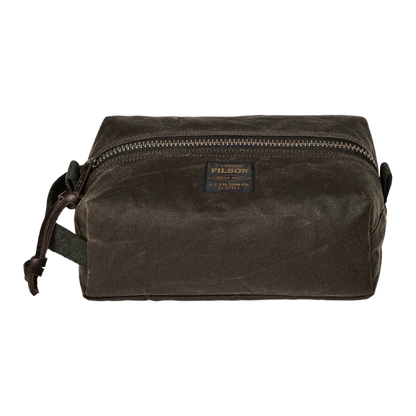 A dark brown waxed canvas pouch bag with a top zipper, a small rectangular Filson brand patch on the front, and a dark strap on the left side, shown against a plain white background.