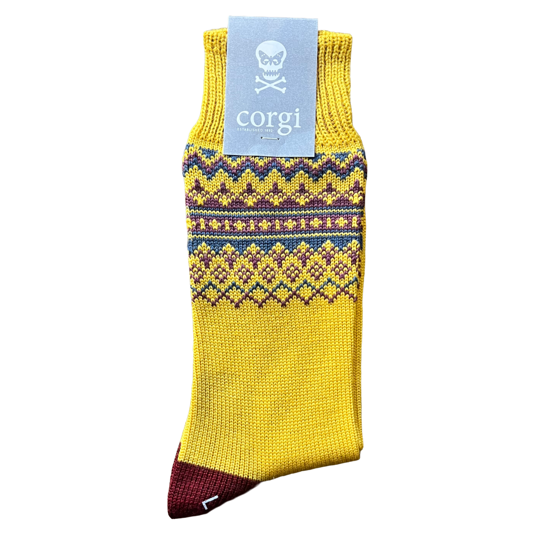 A single yellow knit sock with a blue and purple Fair Isle pattern band, a dark burgundy toe, and a light blue paper tag that reads corgi with a skull logo, shown on a plain white background.