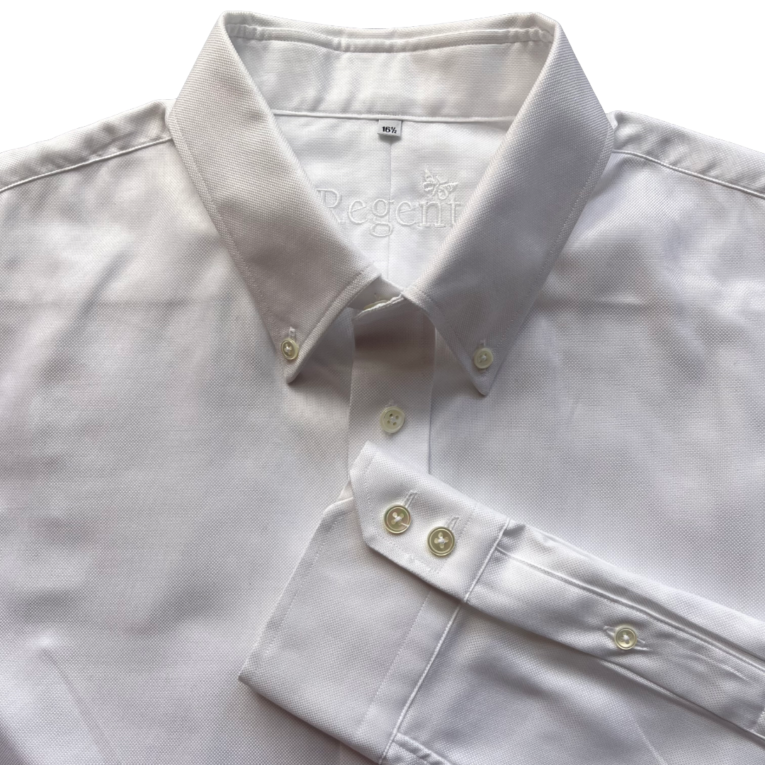 A close-up of a white long-sleeve button-down shirt laid flat, showing the collar, front buttons, and a folded cuff. The inner neck label reads 'Rgnt'.