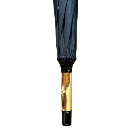 A close-up of an umbrella handle and canopy showing a dark navy blue fabric top and a polished light brown wooden handle with black plastic end caps, isolated on a white background.