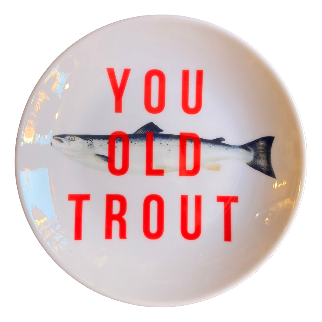 A round white plate featuring a printed salmon fish and the bold red text 'YOU OLD TROUT' on a clean white background.