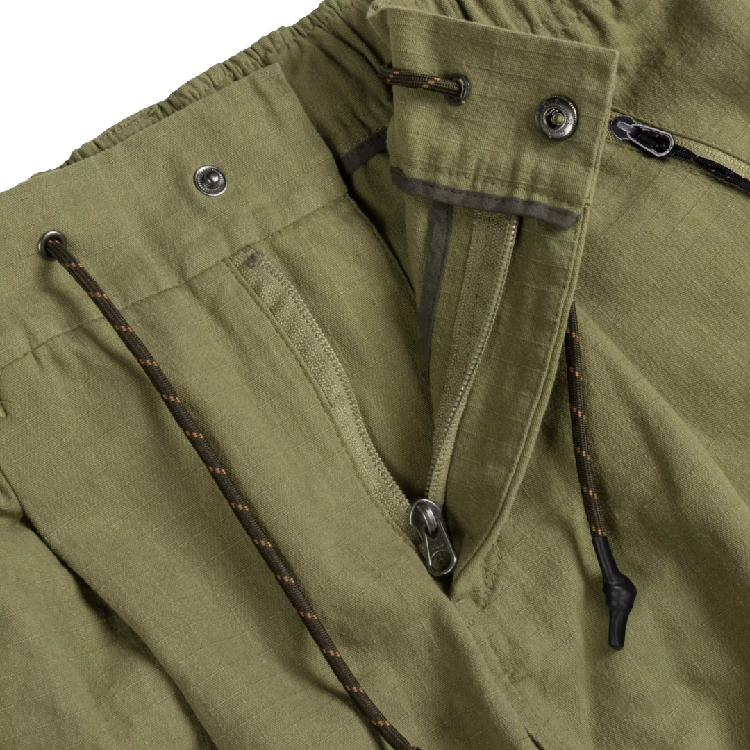 Close-up detail of olive green outdoor pants showing a front zipper pocket, metal snap buttons, and dark drawstring cords with orange flecks.
