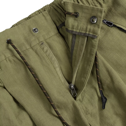 Close-up detail of olive green outdoor pants showing a front zipper pocket, metal snap buttons, and dark drawstring cords with orange flecks.