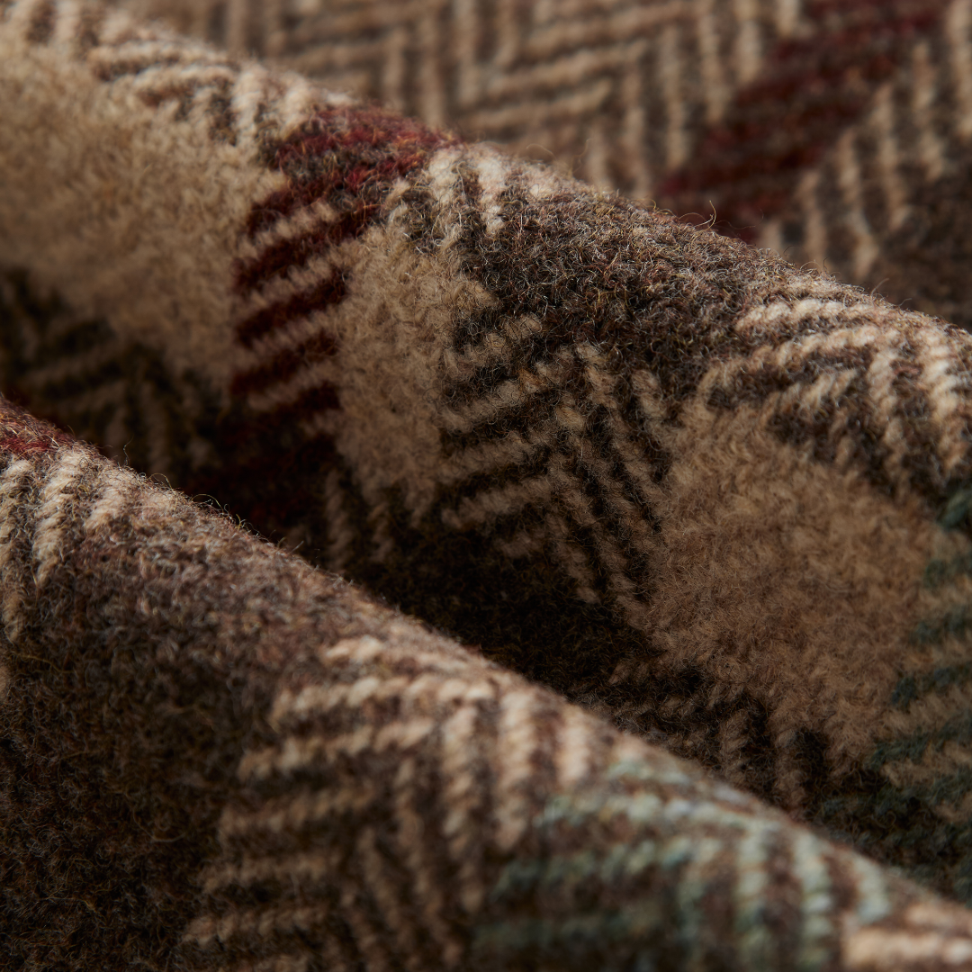Close-up of a textured herringbone wool fabric with a beige, brown, and dark gray pattern, featuring subtle hints of red and teal.