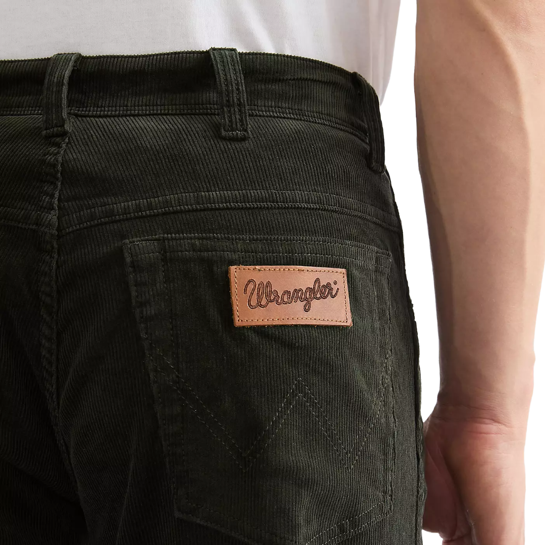 Close-up of a person wearing dark olive green corduroy pants, showing the back pocket with a tan leather Wrangler logo patch.