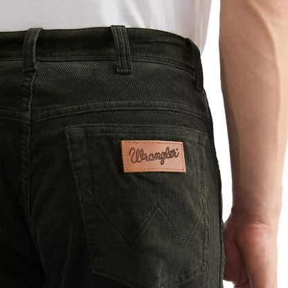 Close-up of a person wearing dark olive green corduroy pants, showing the back pocket with a tan leather Wrangler logo patch.