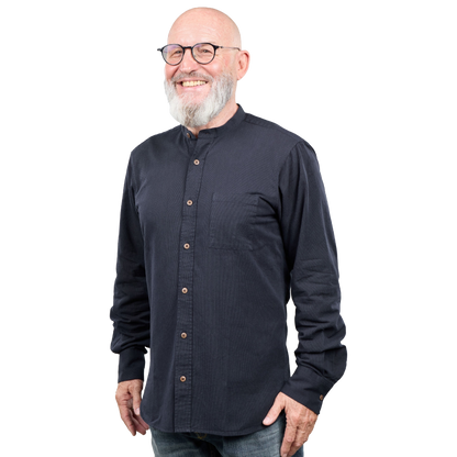 A smiling bald man with a white beard and glasses wearing a dark navy long-sleeve button-up shirt with a mandarin collar, photographed against a solid white background.