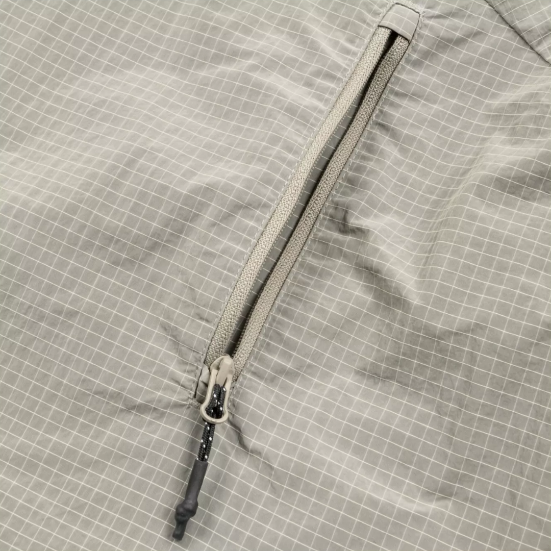 Close-up of a light gray waterproof fabric with a subtle white grid pattern and a matching gray zipper.