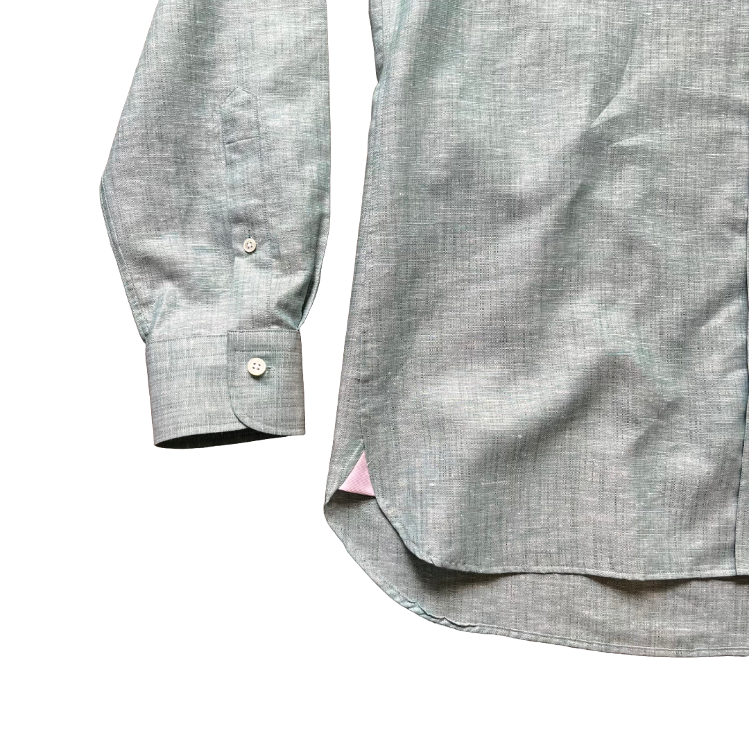 Close-up of a light gray linen-textured button-down shirt showing the sleeve cuff and side hem with a small pink inner lining peeking out, on a white background.