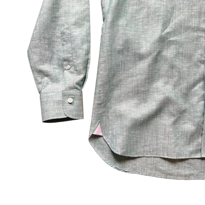 Close-up of a light gray linen-textured button-down shirt showing the sleeve cuff and side hem with a small pink inner lining peeking out, on a white background.