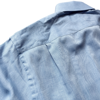 Close-up of a light blue textured fabric garment, showing the collar, shoulder seam, and fine woven texture against a white background.