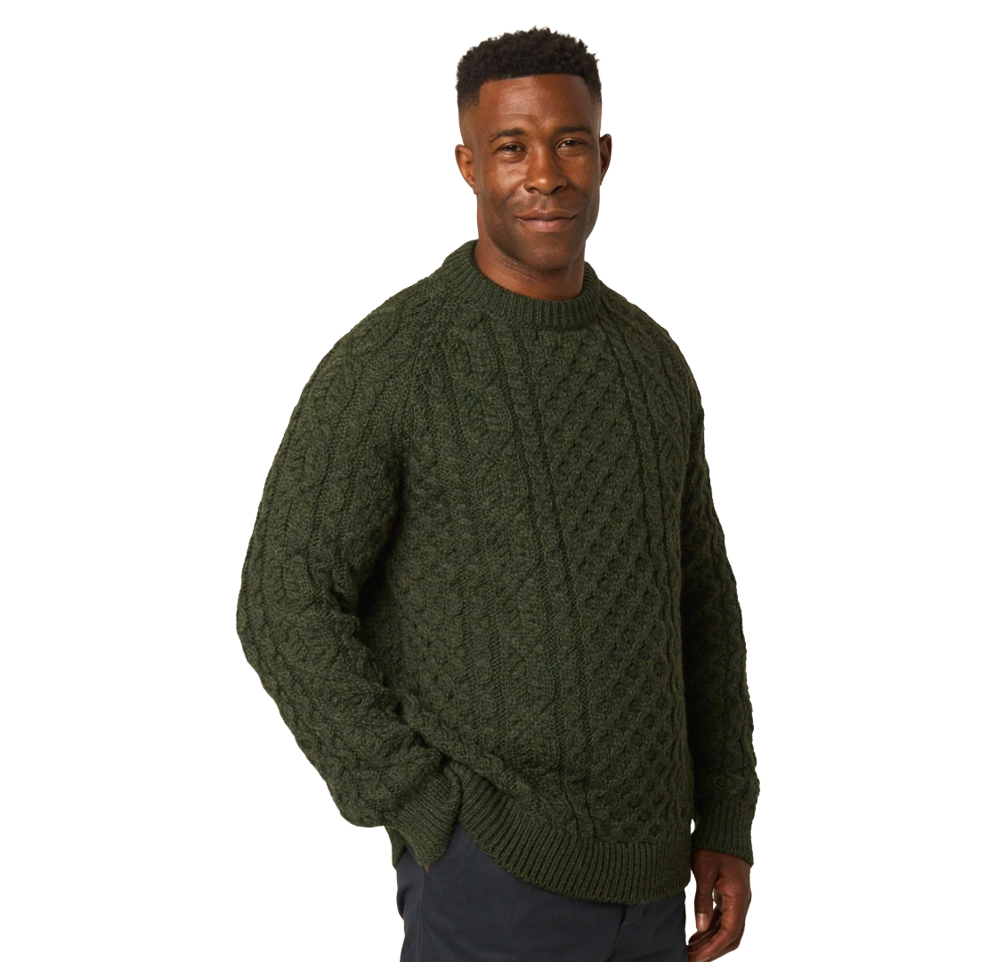 A man wearing a dark olive green cable-knit sweater, standing against a solid white background.