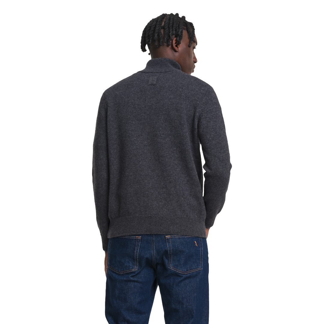 A man viewed from behind wearing a dark charcoal gray knit sweater and blue jeans against a plain white background.