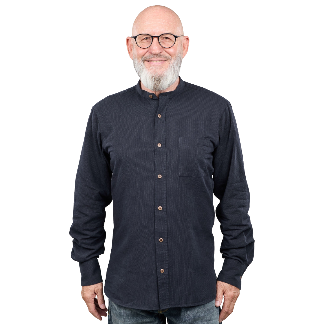 A smiling older man with a white beard and glasses wearing a dark navy long-sleeve button-up shirt with a mandarin collar, photographed against a plain white background.