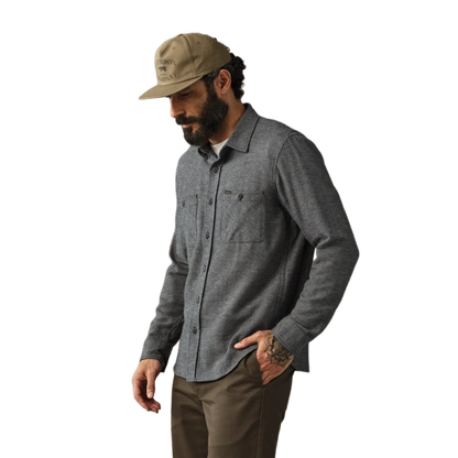 A man wearing a dark gray textured long-sleeve button-up shirt, brown pants, and a tan baseball cap, shown from the waist up against a plain white background.