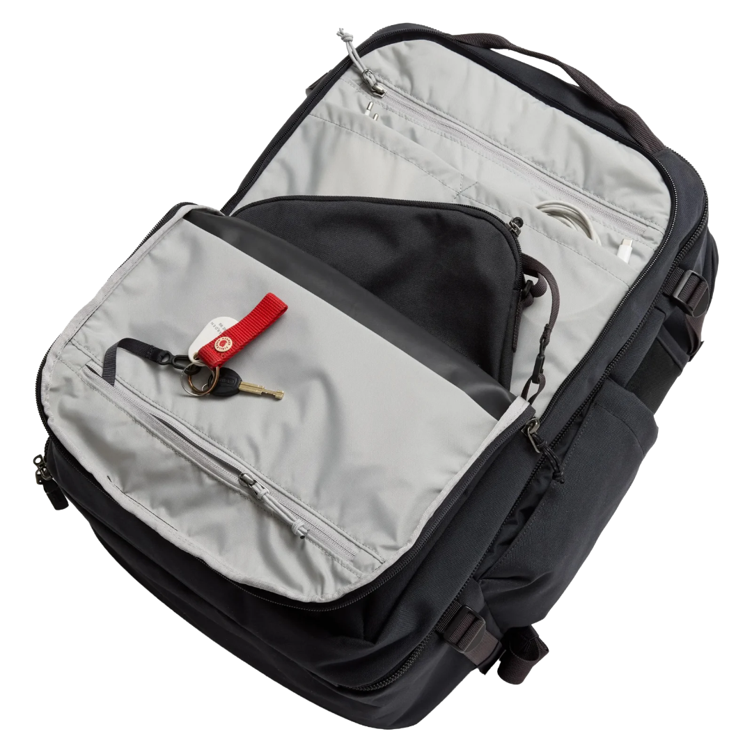 An open black and gray backpack shown from a top-down angle, revealing multiple zippered compartments, interior pockets, and a keychain with keys in the front slip pocket.