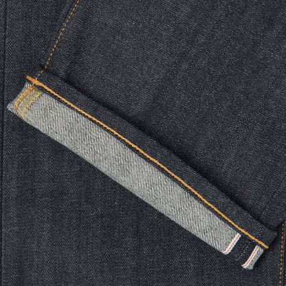 Close-up of a dark indigo denim fabric with a folded hem showing a lighter gray inner lining and orange contrast stitching.