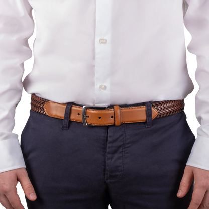 A close-up of a person wearing a white dress shirt, navy pants, and a tan leather belt with a braided brown-and-black waistband, shown against a plain white background.