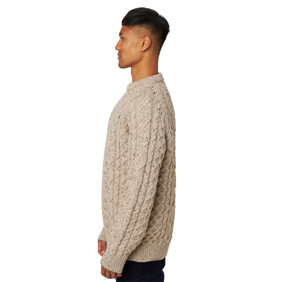 A man shown in profile wearing a beige cable-knit sweater against a plain white background.