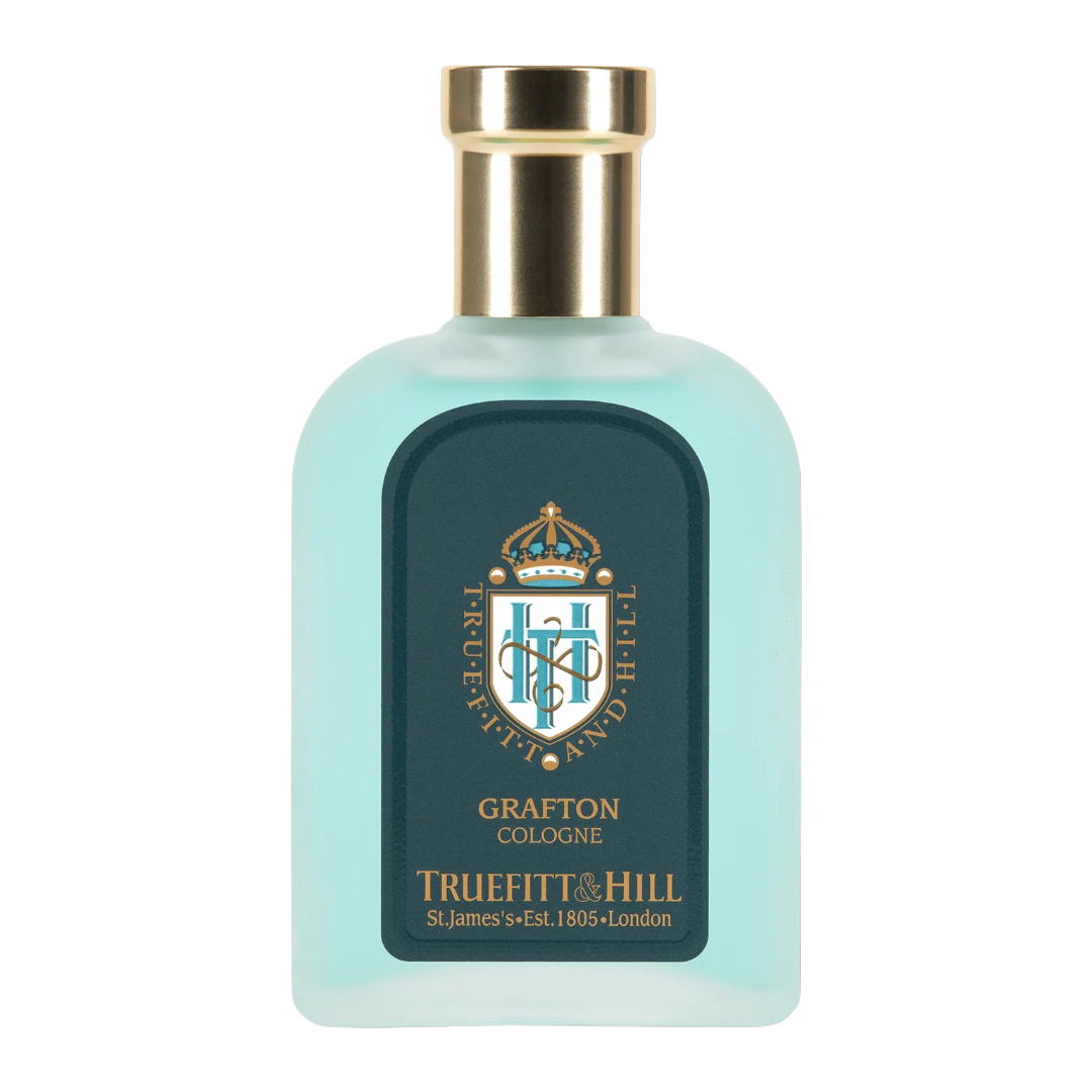 A bottle of Truefitt & Hill Grafton Cologne with a light aqua blue translucent body, a gold metallic cap, and a dark teal label featuring a gold crest.