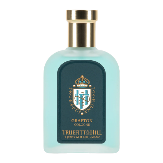 A bottle of Truefitt & Hill Grafton Cologne with a light aqua blue translucent body, a gold metallic cap, and a dark teal label featuring a gold crest.