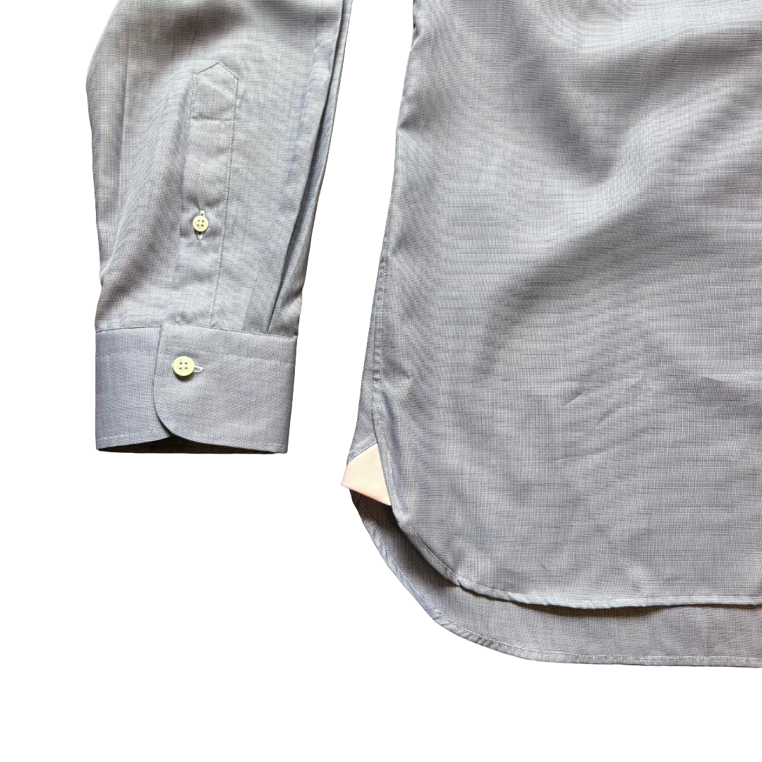 Close-up of a light gray long-sleeve button-down shirt showing the cuff with a single button, a chest pocket, and part of the body of the garment on a white background.