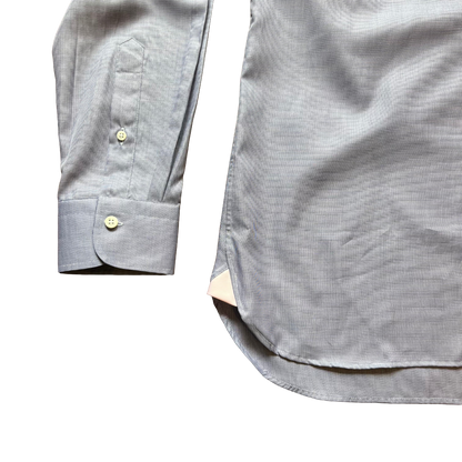 Close-up of a light gray long-sleeve button-down shirt showing the cuff with a single button, a chest pocket, and part of the body of the garment on a white background.