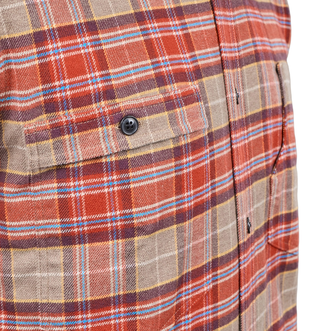 Close-up of a plaid button-up shirt fabric with a chest pocket and black button, showing a pattern of rust red, tan, brown, and light blue stripes.