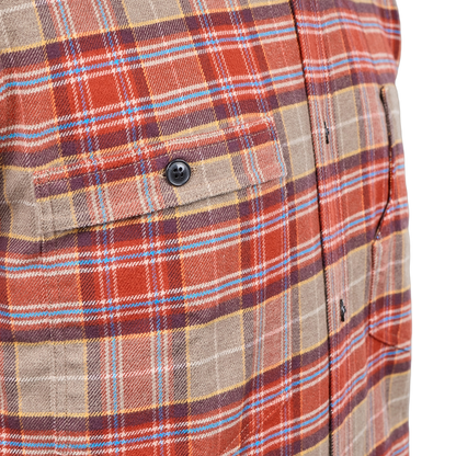Close-up of a plaid button-up shirt fabric with a chest pocket and black button, showing a pattern of rust red, tan, brown, and light blue stripes.