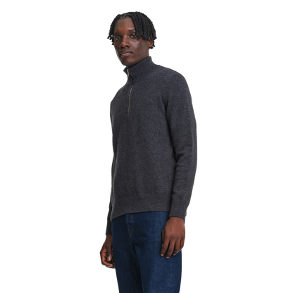 A man wearing a dark gray quarter-zip knit sweater and blue jeans, standing against a plain white background.