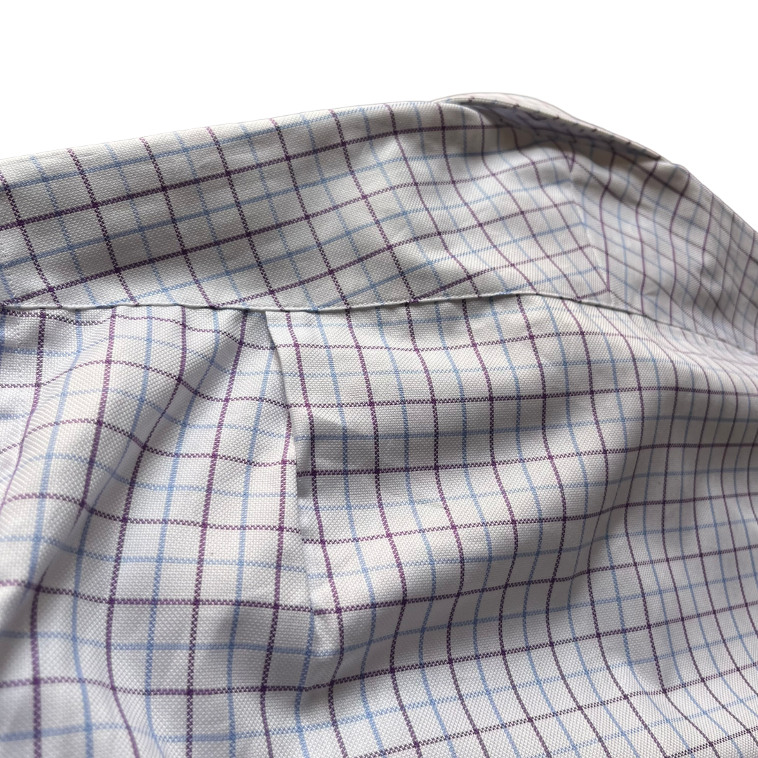 Close-up of a white fabric with a subtle grid pattern in light blue and dark purple, showing a stitched seam and soft folds.