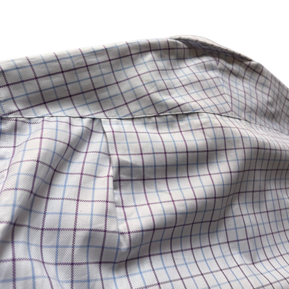 Close-up of a white fabric with a subtle grid pattern in light blue and dark purple, showing a stitched seam and soft folds.
