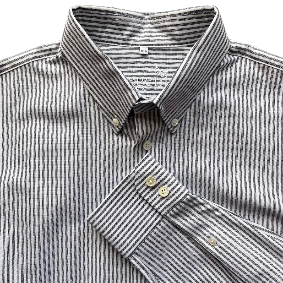 A close-up of a men's long-sleeve button-down shirt with a fine vertical stripe pattern in gray and white. The shirt features a classic pointed collar, a button-down front, and a folded cuff showing the button details.
