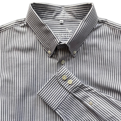 A close-up of a men's long-sleeve button-down shirt with a fine vertical stripe pattern in gray and white. The shirt features a classic pointed collar, a button-down front, and a folded cuff showing the button details.