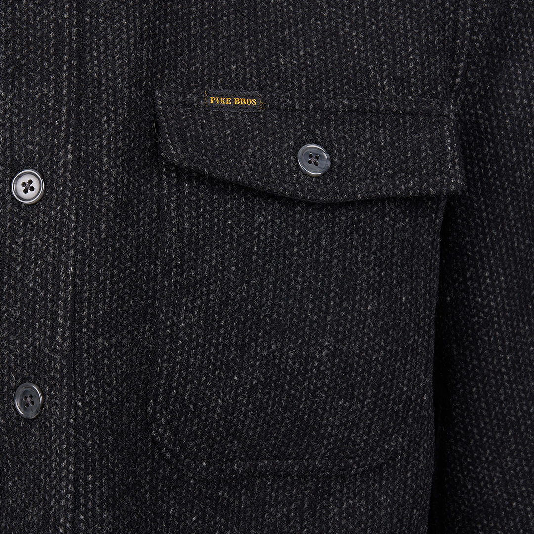 Close-up of a dark charcoal tweed jacket with a chest pocket, button flap, and a small yellow Piqué Boss label.