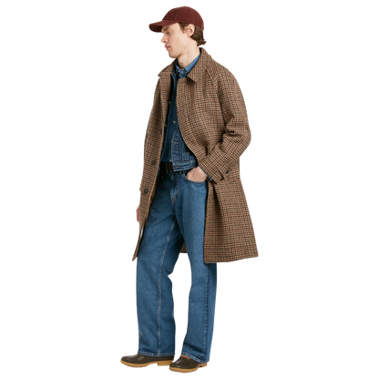 A model wearing a brown and beige plaid overcoat, blue denim shirt and jeans, a maroon baseball cap, and brown shoes, shown in profile against a solid white background.