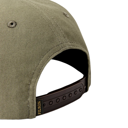 Close-up of the back of an olive green baseball cap with a dark brown adjustable strap and a small gold FILSON logo tag.