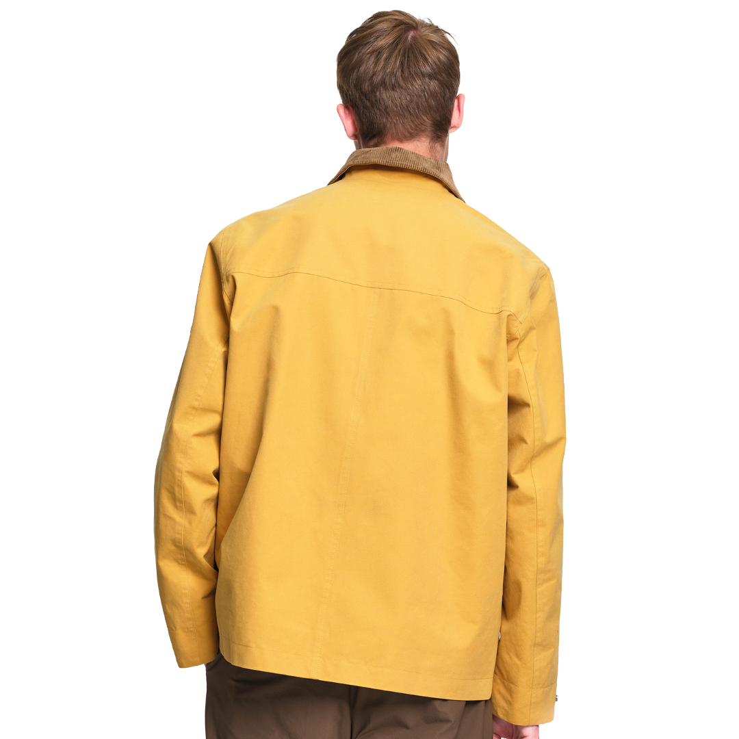 A man viewed from the back wearing a mustard yellow utility jacket with a brown collar, set against a plain white background.