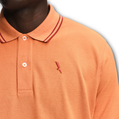 Close-up of an Aigle orange polo shirt with a small logo on a gray background sold at Regent in Salisbury