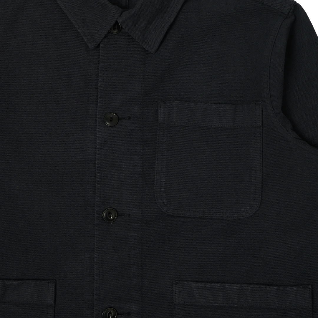 Close-up of a dark charcoal gray or black work shirt jacket, showing the collar, front button closure, chest pocket, and lower patch pockets.