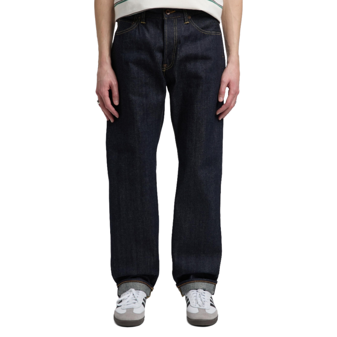 A person wearing dark indigo straight-leg denim jeans, a white and green striped t-shirt, and white sneakers, shown from the waist down against a plain white background.