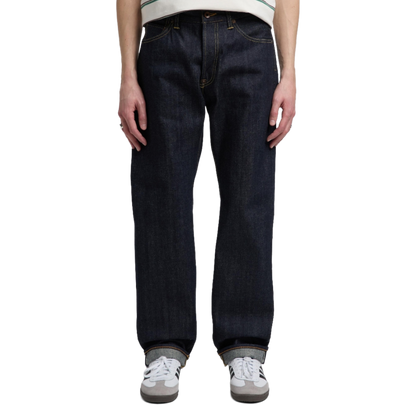 A person wearing dark indigo straight-leg denim jeans, a white and green striped t-shirt, and white sneakers, shown from the waist down against a plain white background.