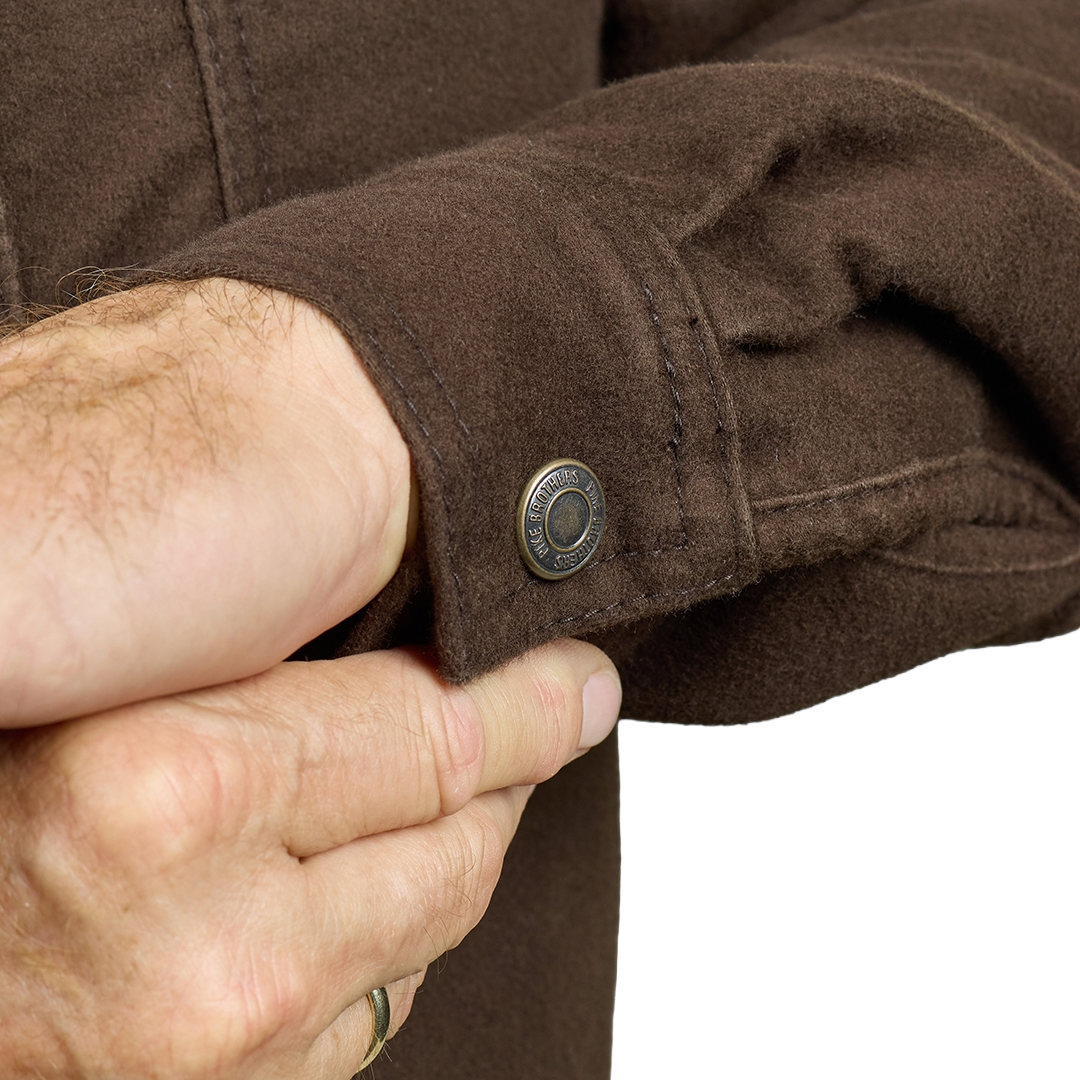 Close-up of a person's hands adjusting the cuff of a brown wool-blend jacket, showing a dark metal snap button with the brand name 'HARLEY-DAVIDSON' visible on the ring.