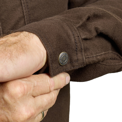 Close-up of a person's hands adjusting the cuff of a brown wool-blend jacket, showing a dark metal snap button with the brand name 'HARLEY-DAVIDSON' visible on the ring.