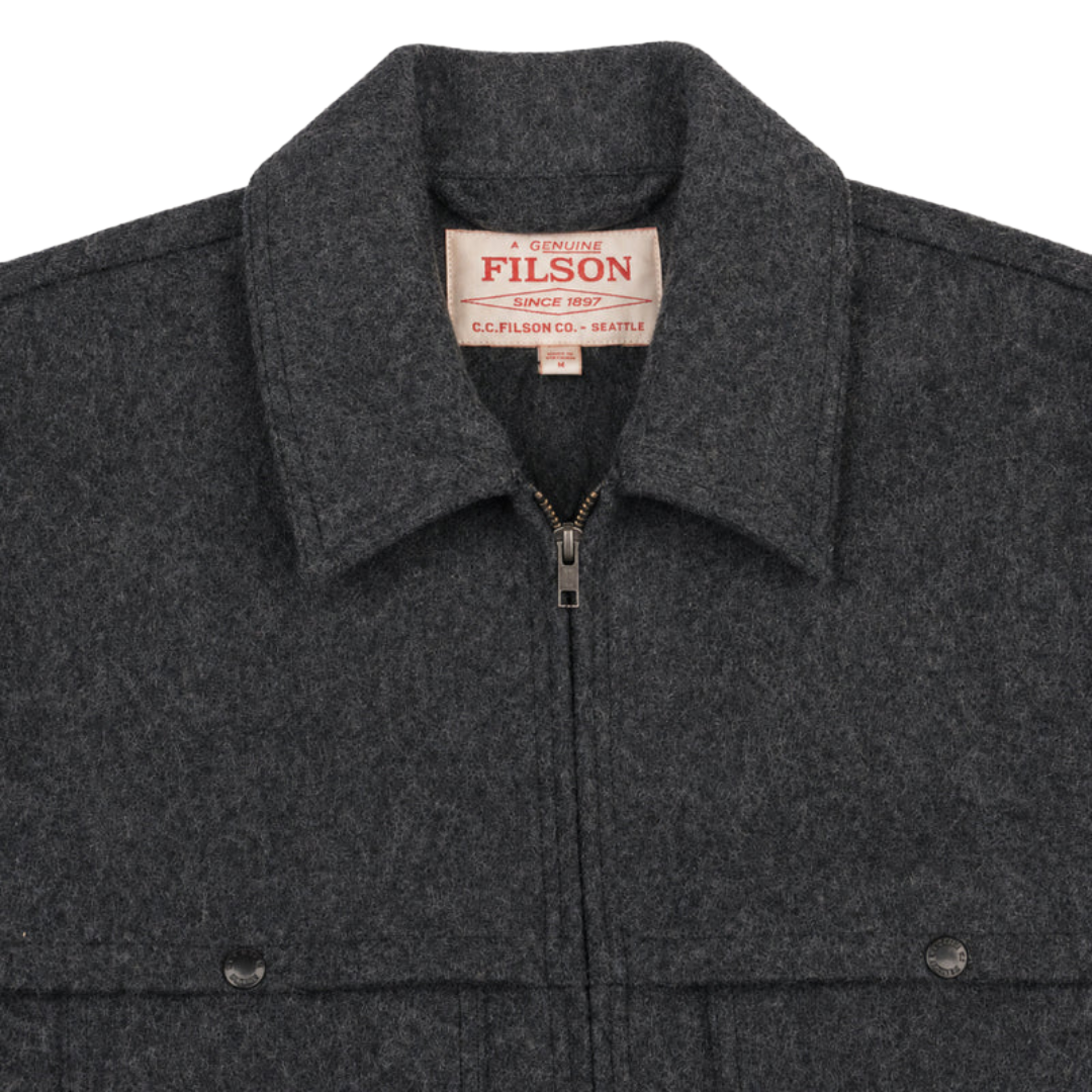 Close-up of a dark charcoal gray wool-blend jacket with a zippered front, pointed collar, and a visible Filson neck label.