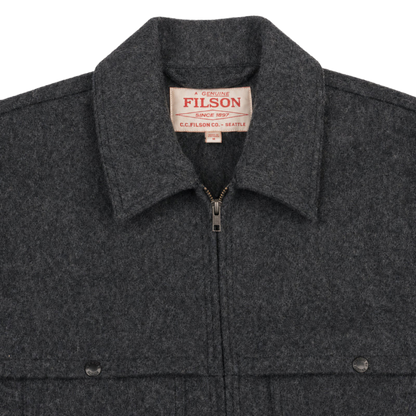Close-up of a dark charcoal gray wool-blend jacket with a zippered front, pointed collar, and a visible Filson neck label.