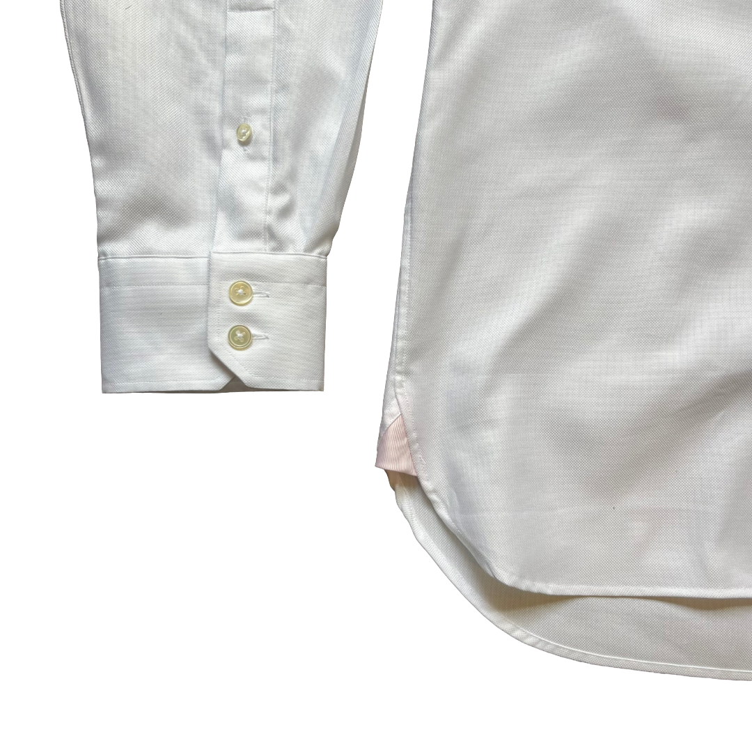 Close-up detail of a white long-sleeve dress shirt showing the buttoned cuff and part of the body of the shirt on a plain white background.