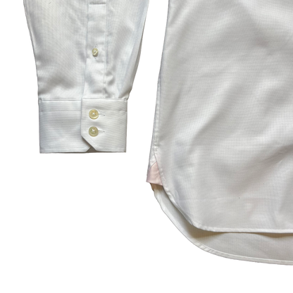 Close-up detail of a white long-sleeve dress shirt showing the buttoned cuff and part of the body of the shirt on a plain white background.